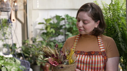 Happy young woman holding bouquet of flower pot showing to camera beautiful arrangement. Portrait girl wearing apron female employee of local small business flower shop 3
