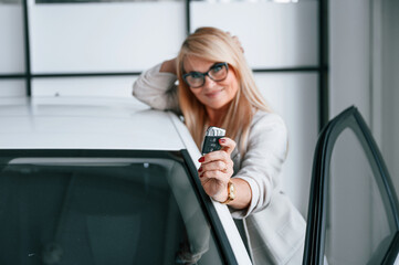 New automobile owner. Woman in white formal clothes is in the car dealership