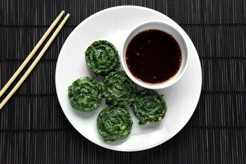 Top view or flat lay packshot Steamed chives dumplings dish served with black soy sauce with a bit of spicy taste from dry chili on black bamboo placemat background next to chopsticks, Food for vegan