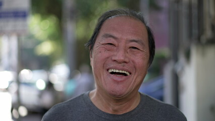 Happy Asian American senior man smiling at camera while walking outdoors. Excited middle aged Japanese person walks in urban street sidewalk