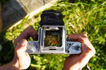 A photographer holding a vintage analog photo camera focusing ajusting taking pictures outside looking through a large square format viewfinder mechanical settings solid metal cogs gagarden background