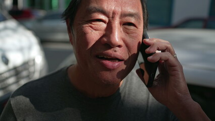 Asian American man speaking on phone in urban street. Portrait of a middle aged person holding smartphone listening