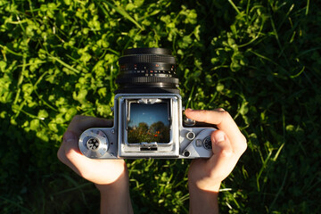 A photographer holding a vintage analog photo camera focusing ajusting taking pictures outside looking through a large square format viewfinder mechanical settings solid metal cogs gagarden background