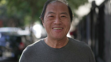 Portrait of a joyful Asian older man smiling at camera. Happy middle aged person walking forward toward camera in street outdoors. closeup face of senior male