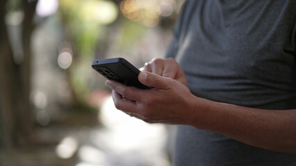 Person using cellphone standing outdoors in city street sidewalk. Closeup hands holding smartphone device texting message