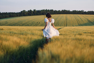 Rear view. Beautiful young bride in white dress is on the agricultural field at sunny day
