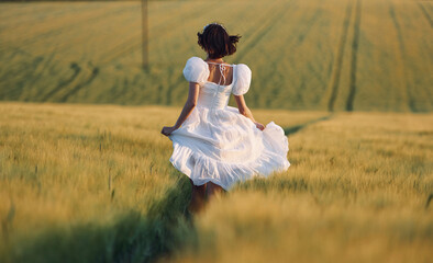 Fototapeta na wymiar Rear view. Beautiful young bride in white dress is on the agricultural field at sunny day