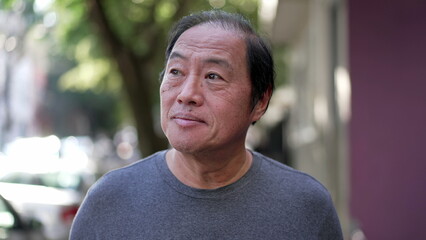 Fototapeta premium One pensive senior man having an idea breakthrough while walking outdoors. Portrait of a contemplative older middle aged Asian person in contemplation