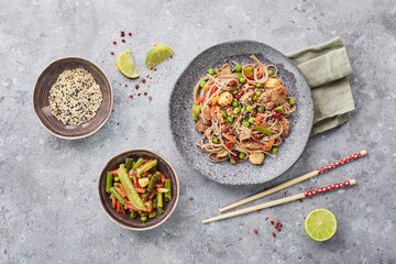 Fototapeta na wymiar Wok with turkey meat, soba noodles, corn, green peas, green beans and carrots served on gray background with chopsticks. Asian food, concept of street food