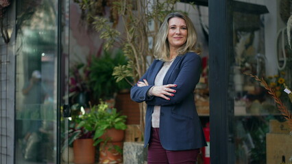 MIddle age entrepreneur smiling standing in the door of her flower shop proud to be the owner of a...