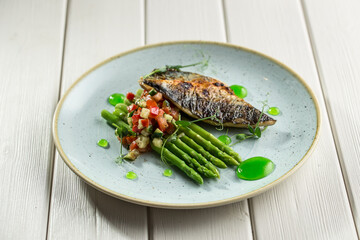 Halved grilled sea bass fish with fresh asparagus and vegetables on plate