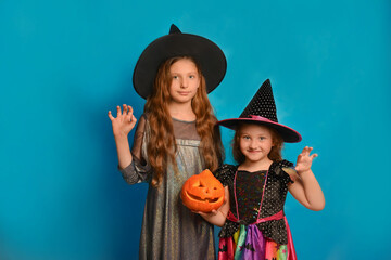 Two cute girls sisters in witches costumes holding Halloween pumpkin, showing Boo gesture and looking at camera on a blue background.

Children wizards celebrating Halloween in carnival costumes.