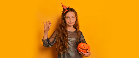 Little witch girl holding Halloween pumpkin, making Boo gesture or doing Boo sign and looking at camera on yellow background with copy space.

Wizard girl wearing small witch hat and sleeve dress.