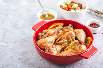 Chicken drumsticks with oranges and thyme baked in red round baking dish