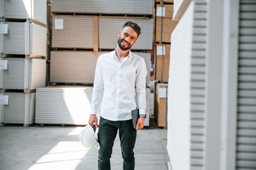 In formal clothes. Storage worker is in the warehouse with bunch of products