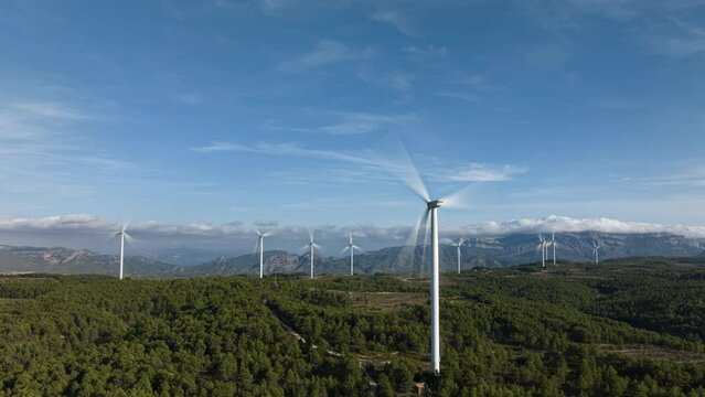 Amazing wind farm scene amongst forest and mountainous terrain. Upwards aerial.
