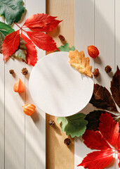 A round paper frame is found along with yellow, red, green fallen leaves, physalis flowers and fir cones on a white wooden background. Autumn, fall, thanksgiving day concept. Flat lay. Copy space.