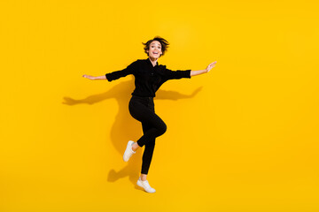 Photo of excited sweet lady wear black shirt jumping high arms hands plane wings empty space isolated yellow color background