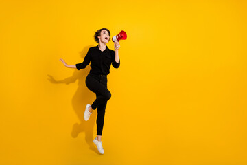 Fototapeta na wymiar Photo of excited funky lady wear black shirt jumping high shouting announcement empty space isolated yellow color background