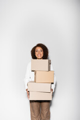 delighted african american woman with curly hair holding delivery boxes on grey.