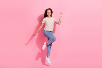 Full length photo of cute friendly girl dressed beige t-shirt jumping high waving hi arm isolated pink color background