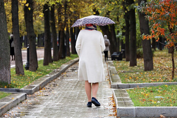 Rain in autumn season, woman with umbrella walking on wet path in city park on people background