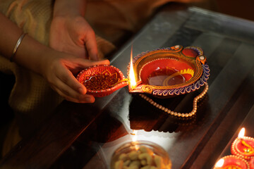 Close up of Young girl lighting Handcrafted Eco Friendly Clay Diya Deep Dia with ambient light...