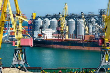 industrial seaport infrastructure, sea, cranes and dry cargo ship, grain silo, bulk carrier vessel and grain storage elevators, concept of sea cargo transportation