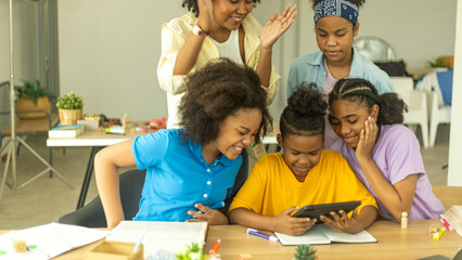 A group of young African kids with their sister use a tablet to communicate with friends. Happy kids use computer for online class under support from a young female teacher. Technology for education