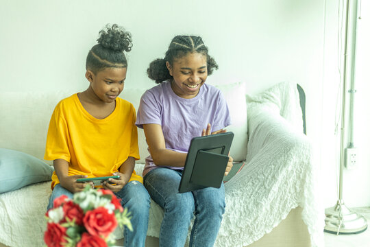 A group of young African kids with their sister use a tablet to communicate with friends. Happy kids use computer at home to socialize with other kids. Technology for education