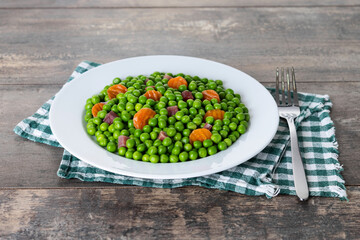 Green peas with serrano ham and carrot on wooden table