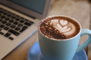 Cup of coffee on a table with laptop in the background. Hot chocolate in a mug. Latte art with a...