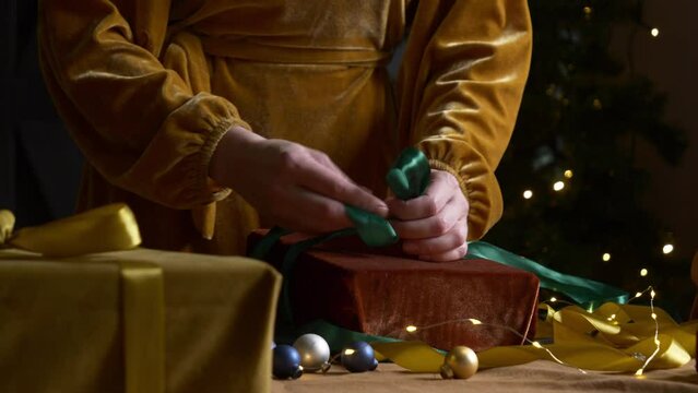 Stylish woman in brown clothes preparing and wrapping gifts in eco fabric on table at home
