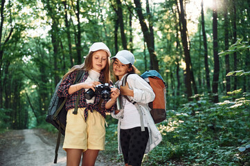 Standing on the footpath. Two girls is in the forest having a leisure activity, discovering new places