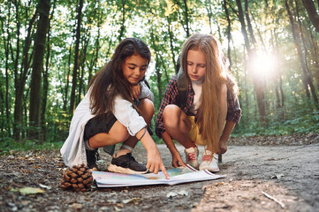 Looking at the map hat is on the ground. Two girls is in the forest having a leisure activity