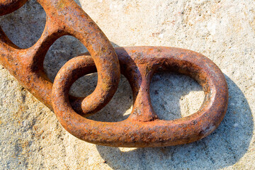 Detail of an old rusty metal chain anchored to a concrete block
