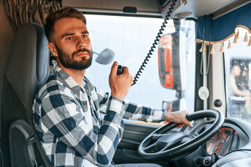 Using radio. Young truck driver is with his vehicle at daytime