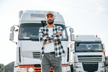 Standing outdoors. Young truck driver is with his vehicle at daytime