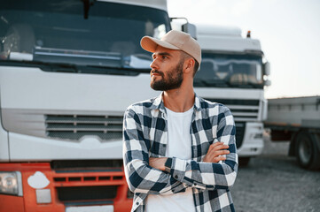 Obraz premium With arms crossed. Young truck driver is with his vehicle at daytime
