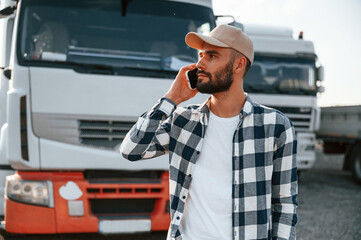 Talking by phone. Young truck driver is with his vehicle at daytime