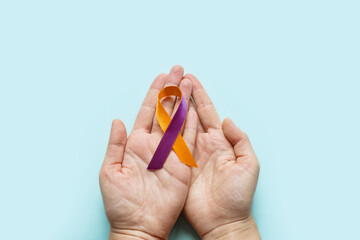 World Psoriasis Day. Woman's hands are holding a purple-orange ribbon on blue background. Treatment of skin diseases, dermatitis, eczema, psoriasis.