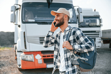 Standing outdoors. Young truck driver is with his vehicle at daytime