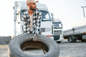 Fototapeta na wymiar With broken tire. Young truck driver is with his vehicle at daytime