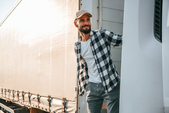 Standing behind the cabin. Young truck driver is with his vehicle at daytime