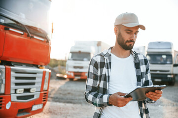 Looking at document in notepad. Young truck driver is with his vehicle at daytime