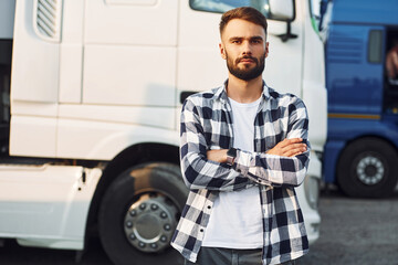 Posing, standing with arms crossed. Young truck driver is with his vehicle at daytime