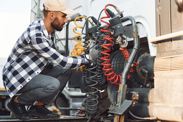 Fixing wires connection. Young truck driver is with his vehicle at daytime