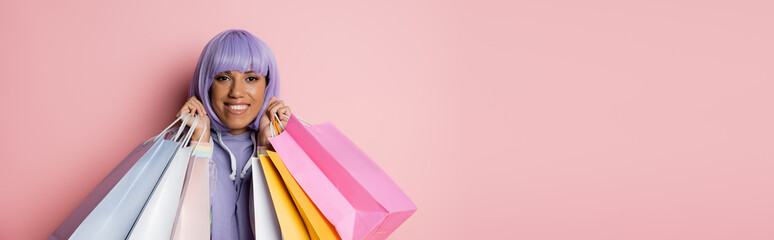 smiling african american woman with purple hair holding shopping bags on pink, banner.