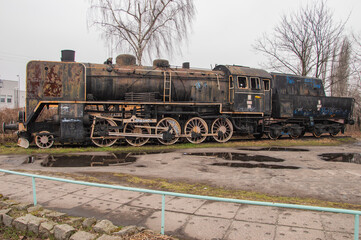 An old and dilapidated historic PKP steam locomotive standing on a siding on a gloomy autumn day. Rail.
