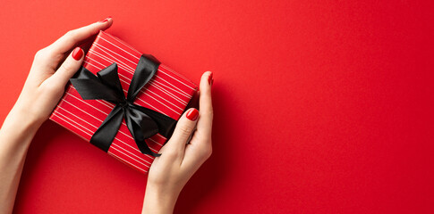 Black friday concept. First person top view photo of young person's hands holding red giftbox with...